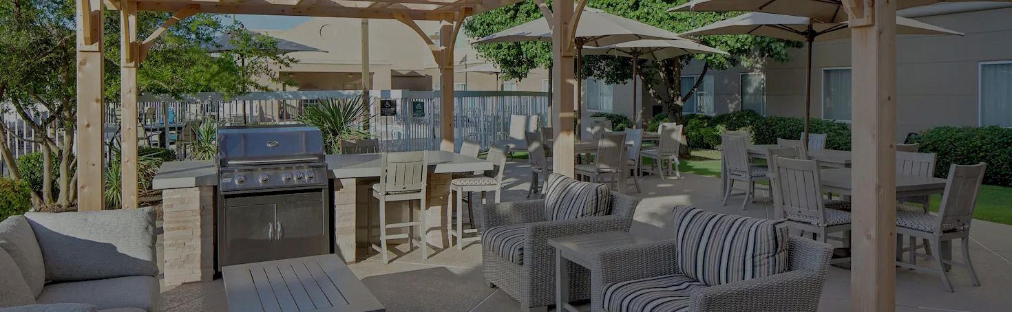 A spacious outdoor patio with wicker seating, a barbecue grill, and several tables under a wooden pergola, perfect for gatherings.
