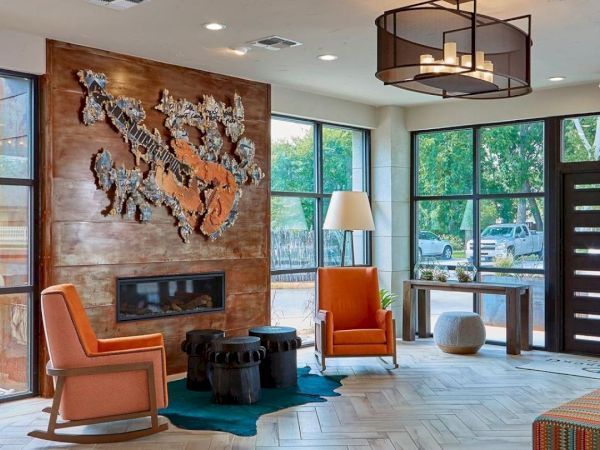 A modern lobby with a wooden feature wall, mounted animal sculpture, orange chairs, large windows, and contemporary lamps, welcoming entrance.