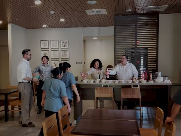 A busy cafe or dining area with people ordering at a counter and others seated or standing around, serving staff behind the counter.