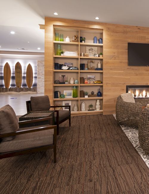 A modern hotel lobby with a cozy seating area, a stone fireplace, wooden wall paneling, and a bookshelf-filled back wall.Top it at 140 characters, always ending the sentence.