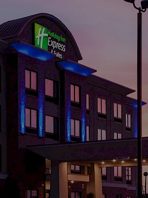 A Holiday Inn Express hotel at dusk, lit blue accents on the façade, with signage and a drive-up entrance.