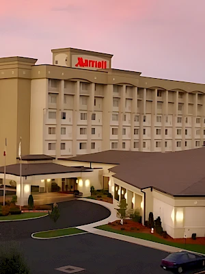 A hotel building with a curved driveway, a smaller entrance area, and a red “Redemption” sign on top, set against a pink sunset.