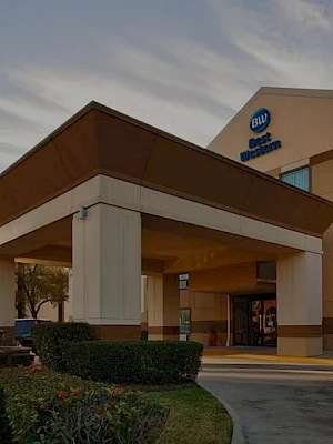 A Best Western hotel exterior at dusk, with a covered entrance, sign, and a multi-story building featuring blue-tinted windows.