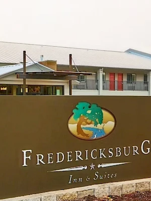 A large sign reads “Fredericksburg Inn & Suites” with a tree emblem; a low, light-colored building and landscaped area behind it.