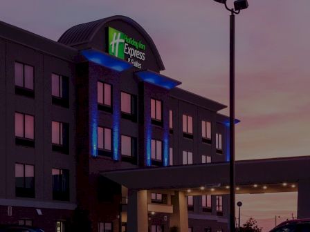 A Holiday Inn Express hotel at dusk with blue exterior lighting and a bright sign, inviting entrance, and a twilight sky behind.