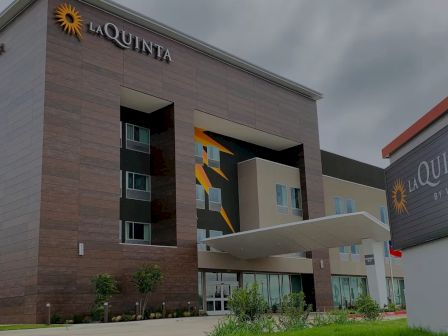 A La Quinta hotel building with a prominent entrance, modern architecture, and a visible sign for La Quinta; outdoor landscaping in front.