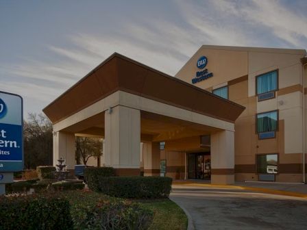 A Best Western hotel exterior at dusk, with a covered entrance, signboard, and a multi-story building; the blue BW logo is prominent.